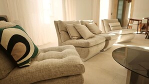 Un salon moderne avec un canapé d’angle, une table basse en verre et un coin repas à l’arrière-plan.