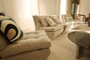 A modern living room with a sectional sofa, a glass coffee table, and a dining area in the background.