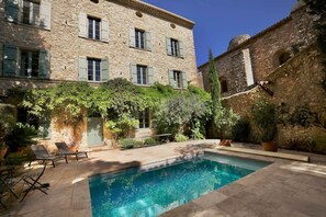 Un bâtiment en pierre doté d’une piscine, d’un espace extérieur aménagé et d’une végétation luxuriante.