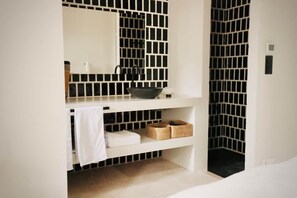 Une salle de bain avec un mur recouvert de carreaux noirs et blancs, un lavabo blanc avec un receveur noir, une serviette et deux paniers en osier posés sur une étagère.