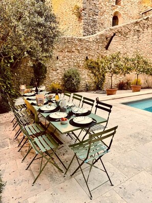 Un espace extérieur aménagé pour les repas, avec un mur en pierre en arrière-plan, une piscine et des plantes en pot.