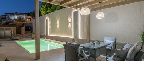 An outdoor patio with a pool, wicker furniture, and a hanging light fixture.