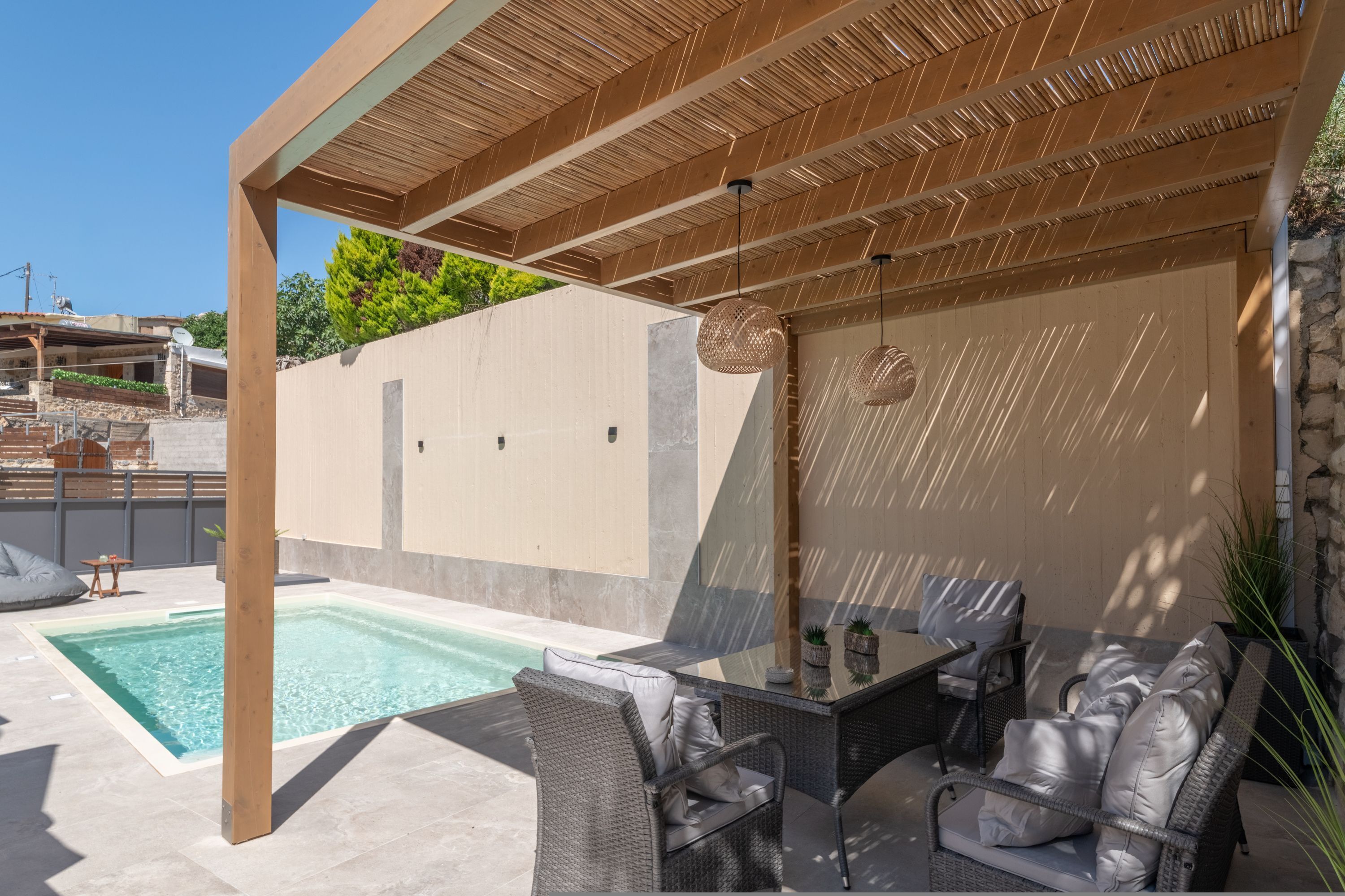 A covered outdoor area with a pool, wicker furniture, and a stone wall.