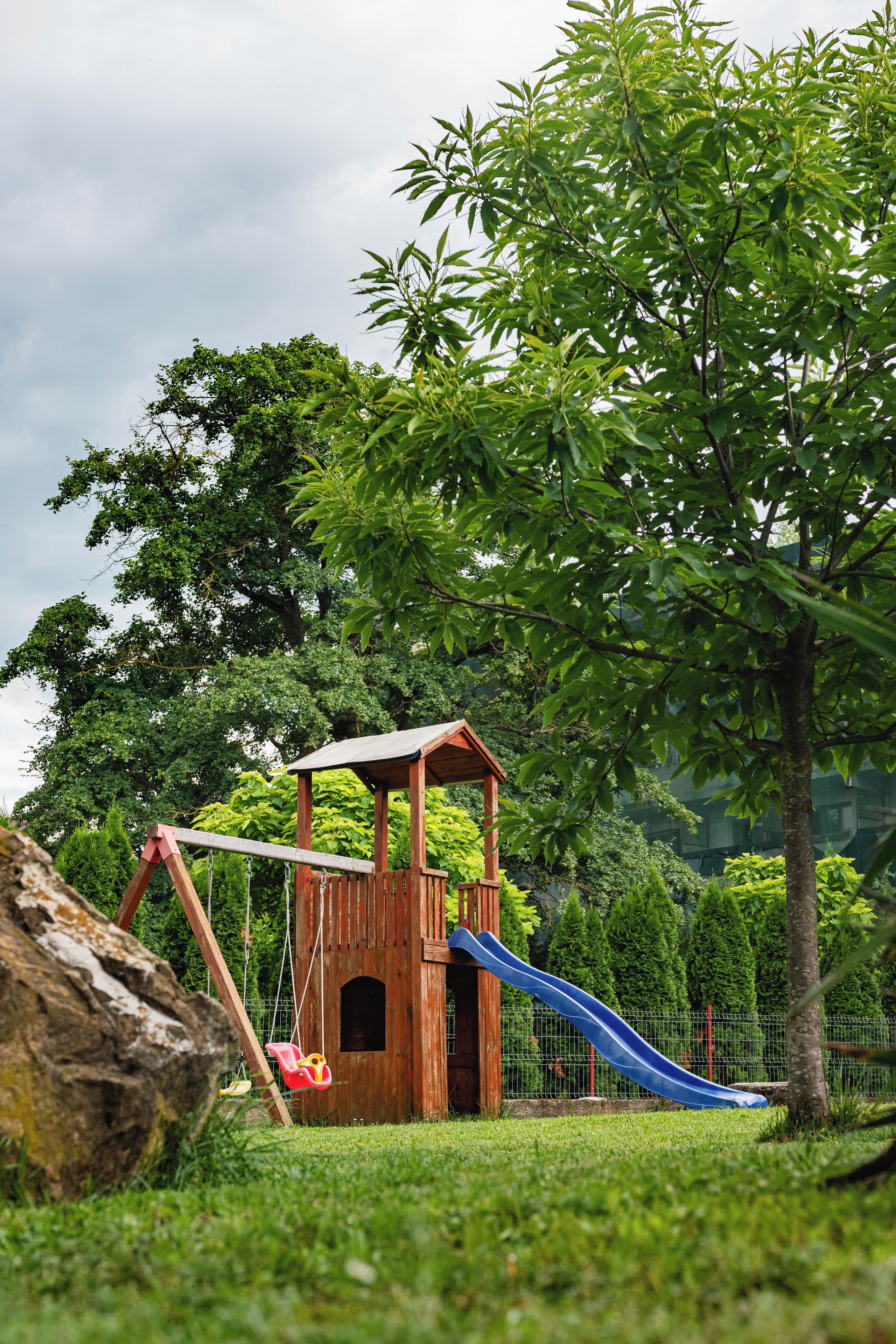 Een houten speeltuintje met een glijbaan en schommel in een park.