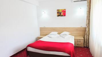 A hotel room with a bed, a nightstand, a wall-mounted air conditioner, and a small picture of flowers.