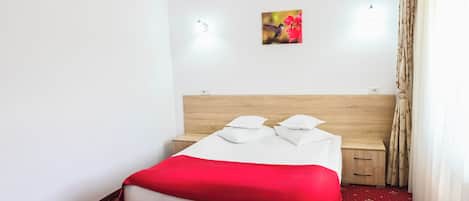 Habitación de hotel con cama, mesita de noche, aire acondicionado de pared y una pequeña imagen de flores.