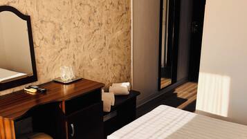 Une chambre d’hôtel avec un lit, un bureau, une chaise, un miroir et une salle de bain visible à travers une porte ouverte.