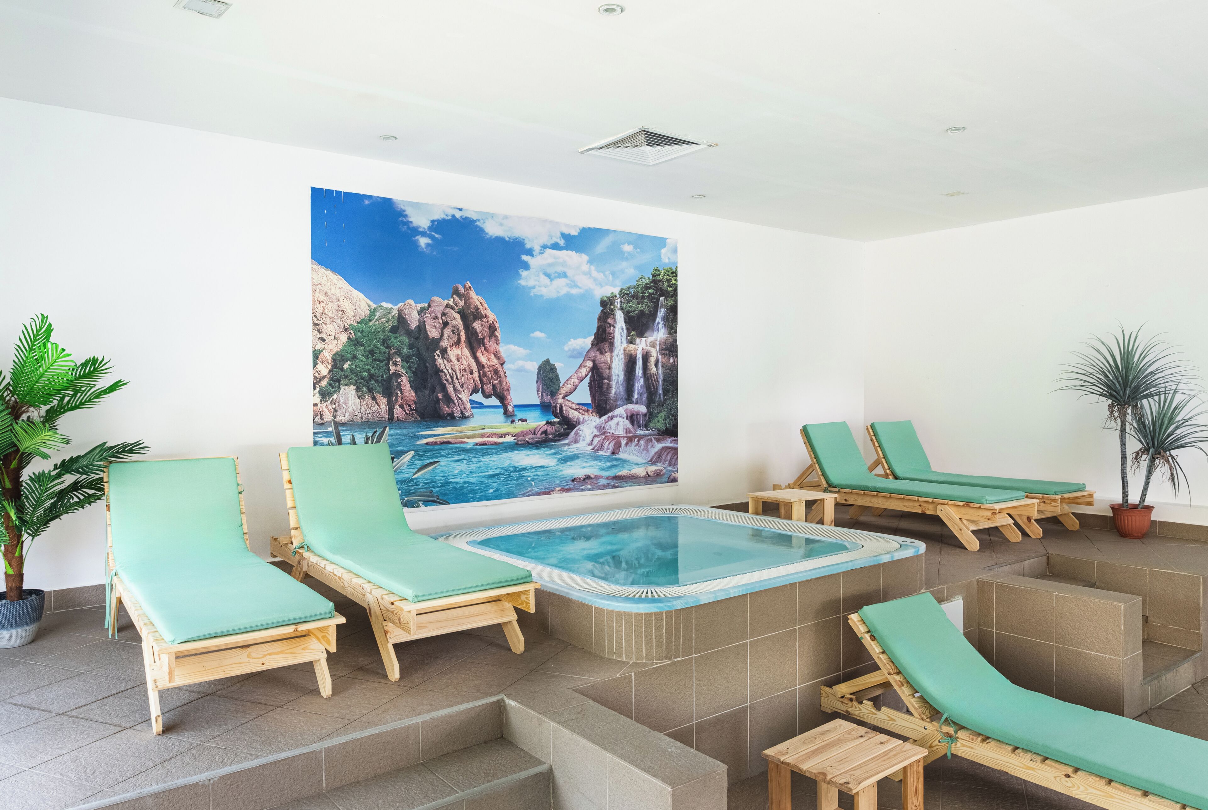 Un área de spa con un jacuzzi, sillones de madera para relajarse y un gran mural de un paisaje costero.