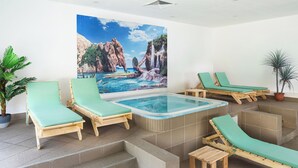 Un área de spa con un jacuzzi, sillones de madera para relajarse y un gran mural de un paisaje costero.