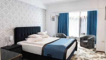 Ein Hotelzimmer mit Bett, Nachttisch, Stuhl, kleinem Tisch und einem Fenster mit Vorhängen.