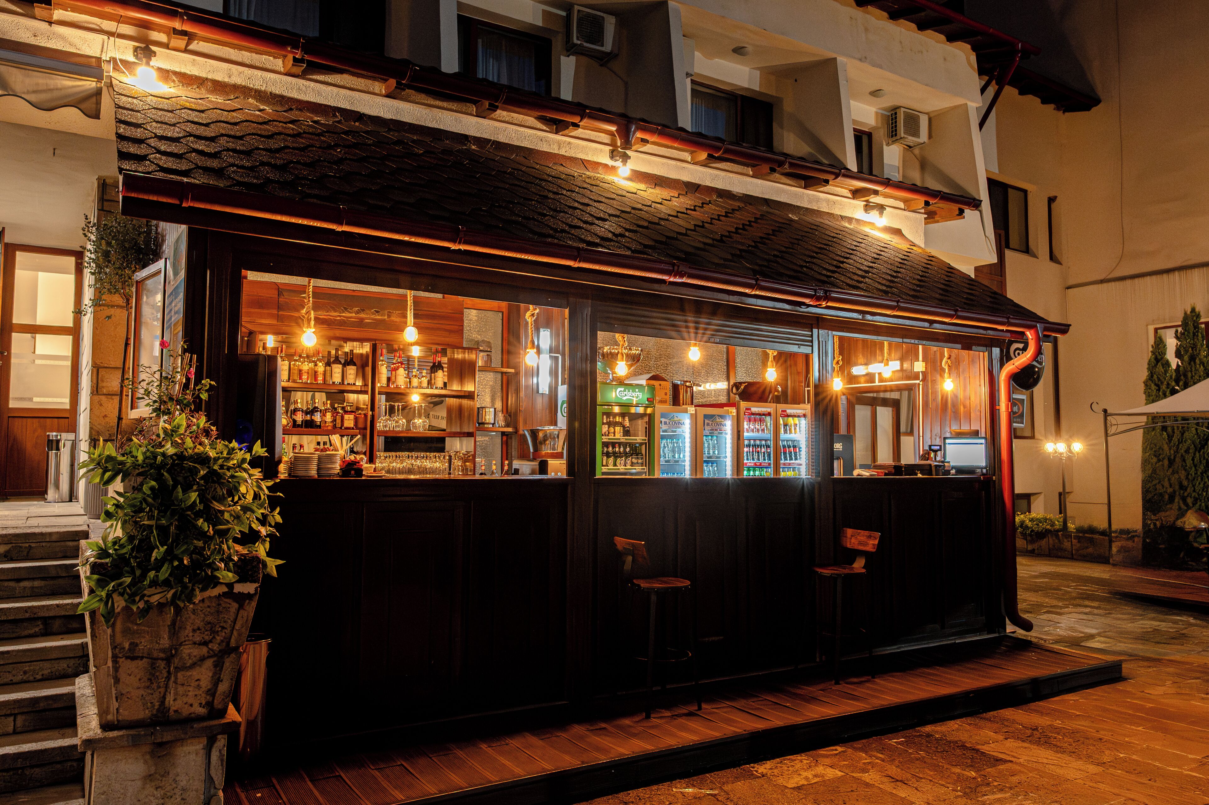 A bar with a wooden exterior, a counter with bottles, and a seating area.