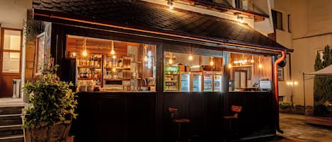 A bar with a wooden exterior, a counter with bottles, and a seating area.