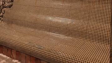 Un mur de briques avec un motif texturé, un banc recouvert d’un treillis métallique et un mur de pierres.