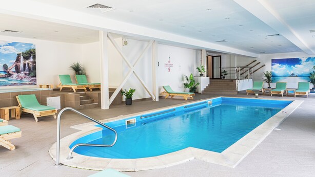 Una piscina interior con sillas de descanso, una escalera y arte en las paredes.