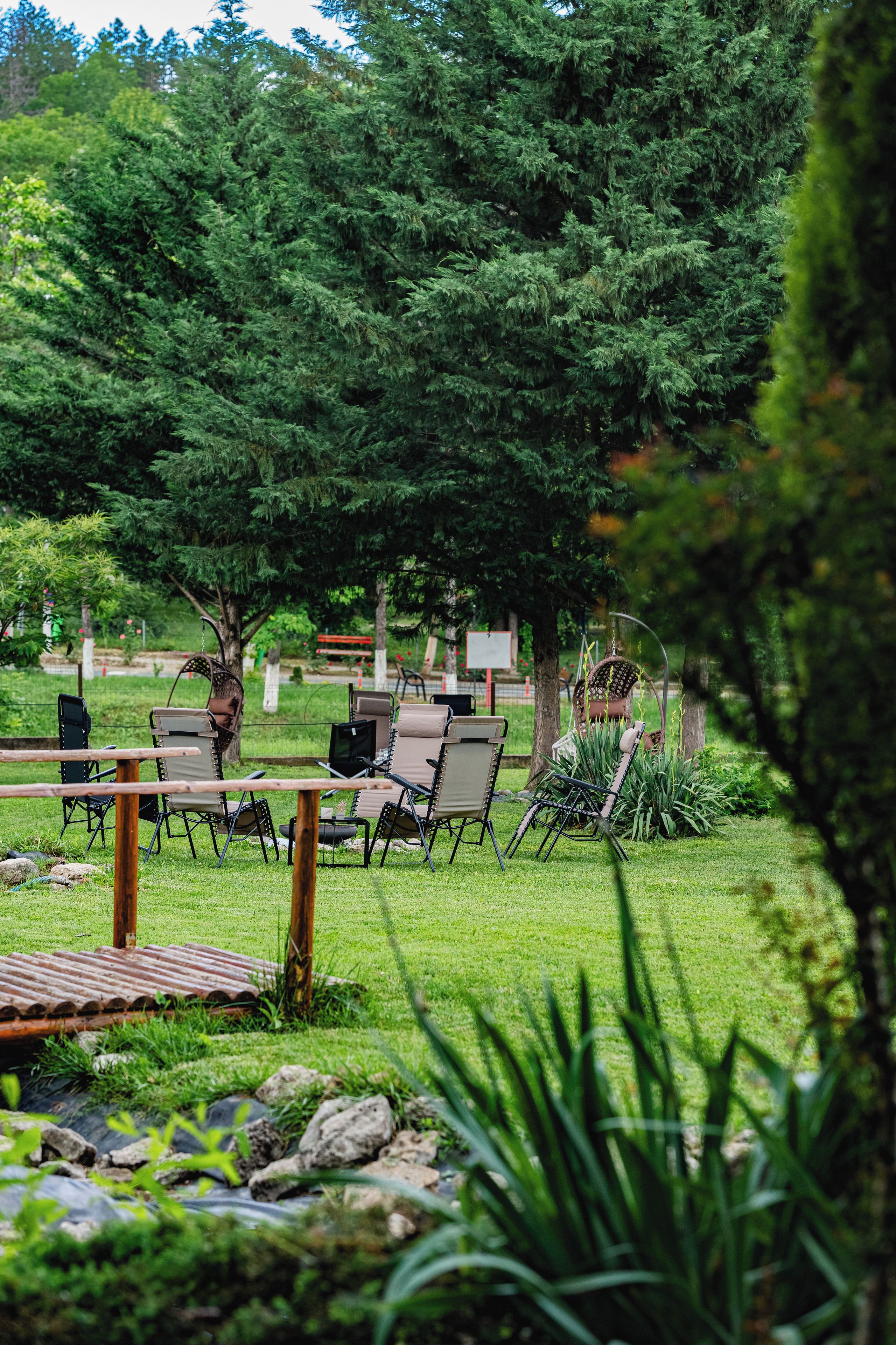 Un espace extérieur aménagé avec des chaises et des tables, entouré de verdure et d’arbres.