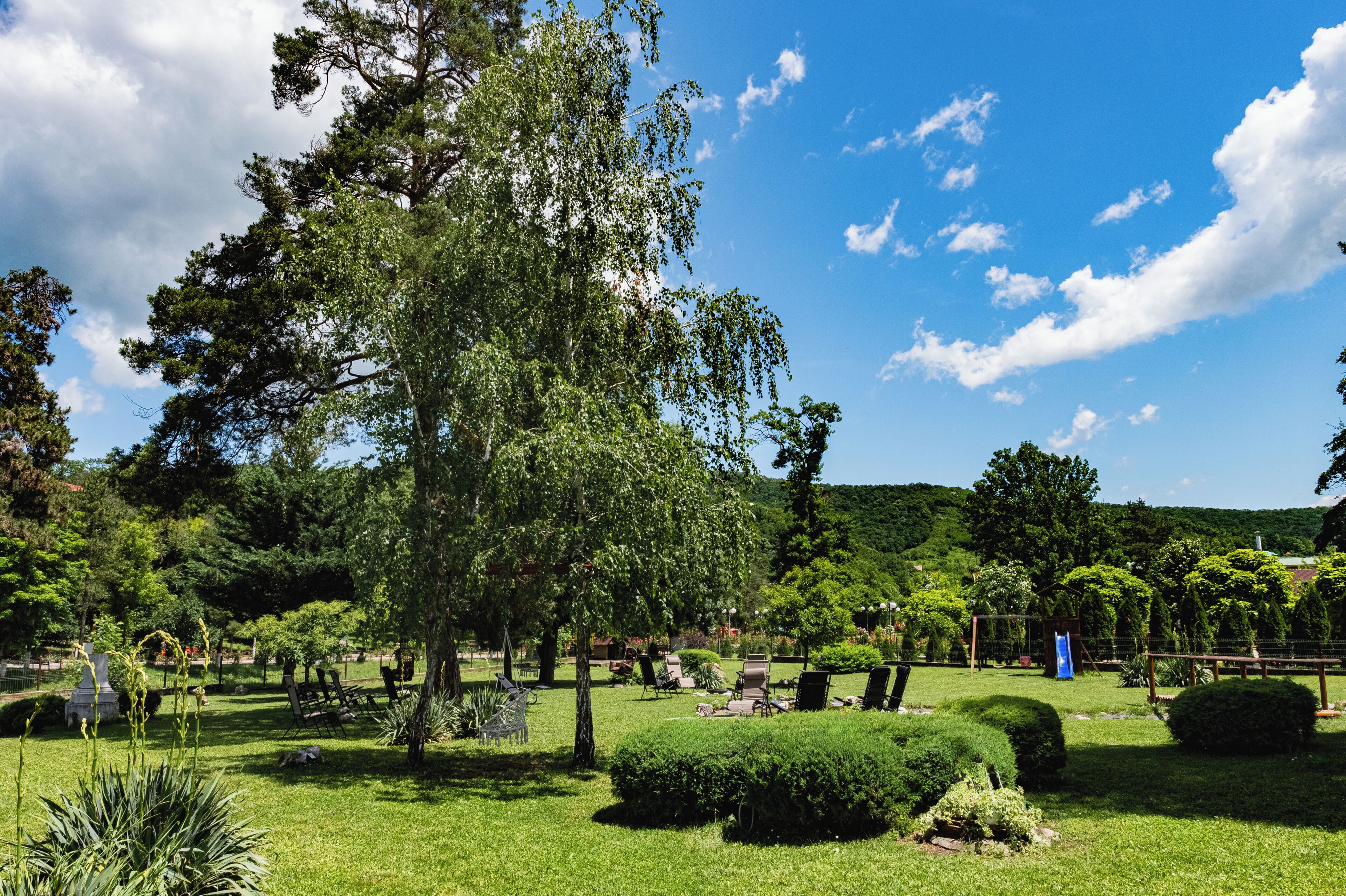 A well-maintained garden with various trees, a playground, and seating areas.