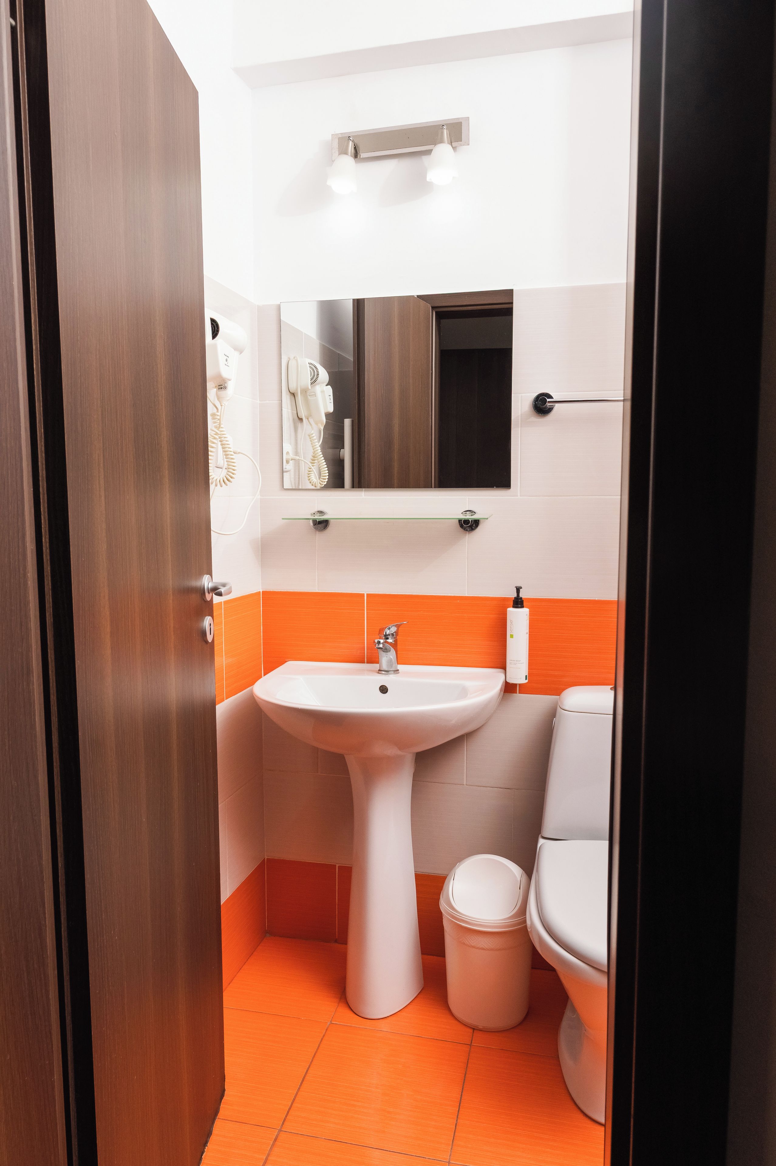 A bathroom with a white sink, a mirror, and an orange-tiled floor.