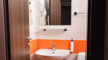 A bathroom with a white sink, a mirror, and an orange-tiled floor.