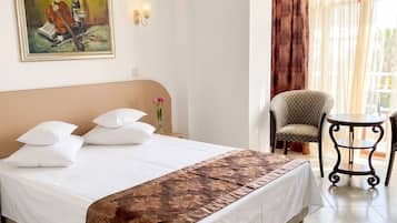 A hotel room with a bed, a chair, a painting, and a window with curtains.