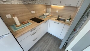 A compact kitchen with a wooden countertop, a sink, and white cabinets. - La Corniche Large Studio (Courseulles-sur-Mer)