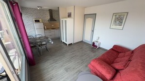 A compact living space with a dining area, kitchenette, and a red sofa. - La Corniche Large Studio (Courseulles-sur-Mer)