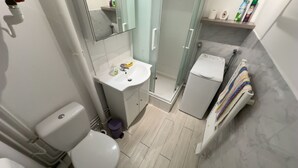 A bathroom with a toilet, sink, shower, and a small white appliance, possibly a heater or dryer. - La Corniche Large Studio (Courseulles-sur-Mer)