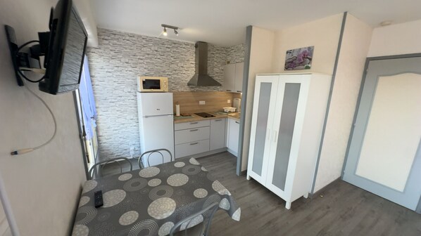 A compact kitchen with a microwave, refrigerator, and a small dining table with chairs. - La Corniche Large Studio (Courseulles-sur-Mer)