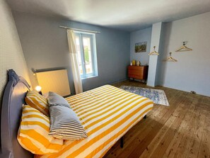 Un dormitorio con una cama, un aparador, un radiador, una ventana y un perchero de pared.