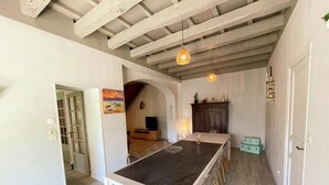 A dining area with a long table, chairs, a ceiling with exposed beams, and pendant lighting.