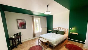 A bedroom with a bed, a nightstand, a chair, a window with curtains, a painting on the wall, and a green accent wall.