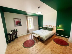 Une chambre à coucher comprenant un lit, une table de chevet, une chaise, une fenêtre avec des rideaux, un tableau accroché au mur et un mur d’accent de couleur verte.