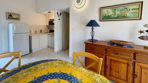 A compact kitchen with a refrigerator, a sink, and cabinets. There is a dining area with a table and chairs. - Charming house near sea - 4 guests (Saint-Jean-de-Monts)