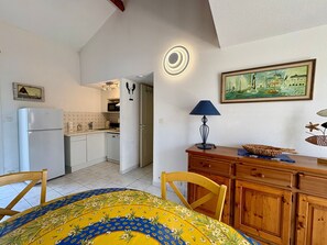 Eine kleine Küche mit Kühlschrank, Spüle und Schränken. Es gibt eine Essecke mit Tisch und Stühlen.