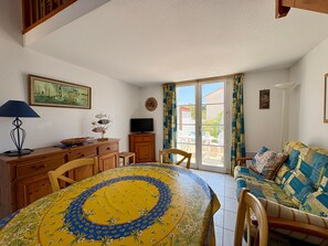 Ein Zimmer mit Esstisch, Stühlen, einer Couch, einem Fernseher und einem Fenster mit Vorhängen.