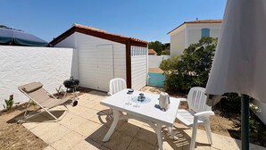 A patio with a table and chairs, a grill, and a white wall. - Charming house near sea - 4 guests (Saint-Jean-de-Monts)