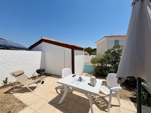 Eine Terrasse mit Tisch, Stühlen und einem Grill, sowie eine weiße Wand.