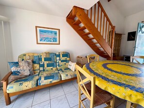Ein Zimmer mit einer Couch, einem Esstisch, einer Holztreppe und einem gerahmten Bild an der Wand.