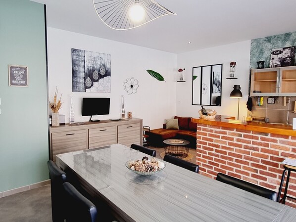 A modern kitchen with a brick accent wall, a dining area with a large table, and a living space with a sofa and artwork.