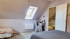 A bedroom with a sloped ceiling, a skylight, a bed, a desk, and a crib.