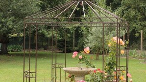 A garden with a metal gazebo structure, a stone fountain, and blooming roses.