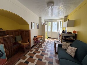 Ein gemütliches Wohnzimmer mit Kamin, einer Couch, einem Esstisch und einem durch eine offene Tür einsehbarer Küchenbereich.