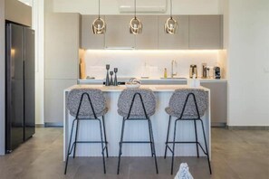 Une cuisine moderne dotée d’un îlot central, de tabourets de bar, de luminaires suspendus et d’un réfrigérateur en acier inoxydable.