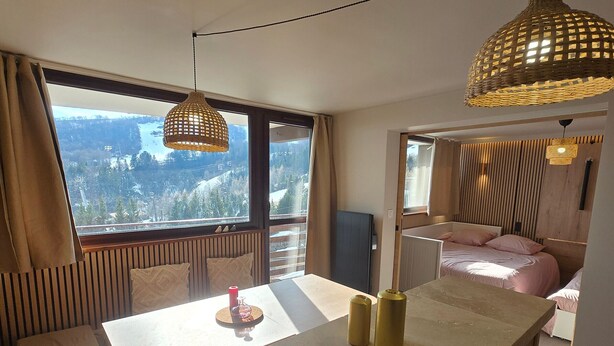 A modern hotel room with a large window, a dining area, and a bed with a view. - Apartment at the foot of the slopes - 6 guests (Besse-et-Saint-Anastaise-Super Besse)