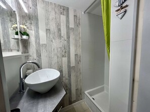 Ein Badezimmer mit einem weißen Waschbecken, einer Dusche und einer Wandverkleidung aus Holz.