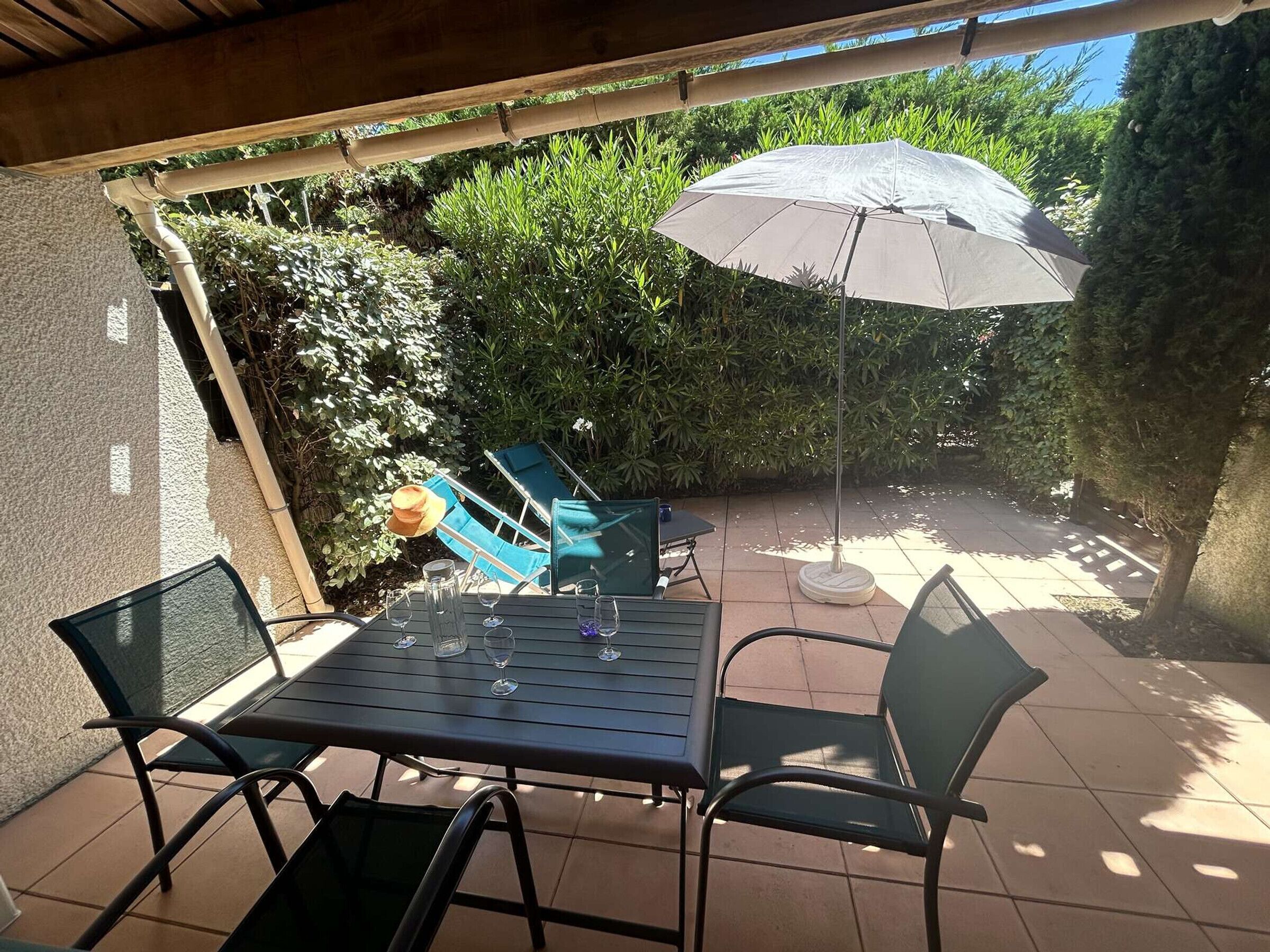 Eine Terrasse im Freien mit Tisch und Stühlen, einem überdachten Bereich und Blick auf einen Garten.