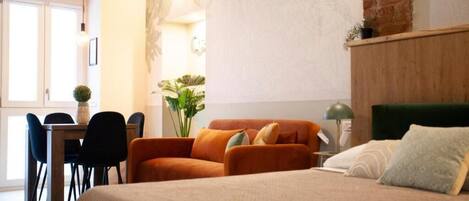A room with a bed, a desk, chairs, and a large window.