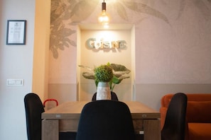 A dining area with a wooden table, black chairs, a red chair, a wall-mounted sign reading 'CUISINE,' and a decorative plant.