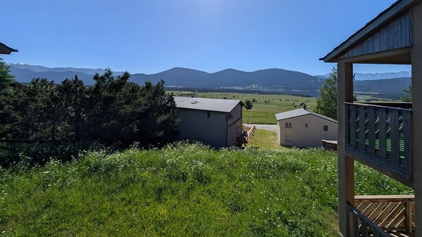 A view from a covered outdoor area with a wooden deck, overlooking a grassy field and distant mountains under a clear sky. - Apartment mountain and lake view - 6 guests (Les Angles)