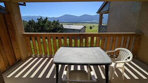 A wooden deck with a table and chairs, a view of mountains, and a building in the background. - Apartment mountain and lake view - 6 guests (Les Angles)
