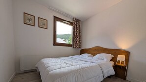 A bedroom with a bed, a nightstand with a lamp, a window with curtains, and two framed pictures on the wall. - Apartment mountain and lake view - 6 guests (Les Angles)